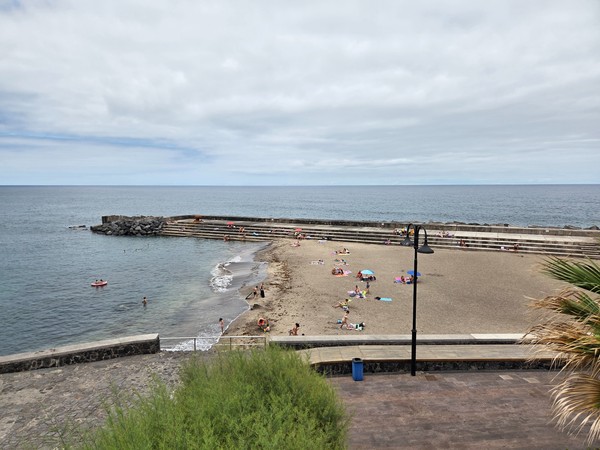 Feinsandiger Stadtstrand neben den Naturpools von Bajamar mit Badenden und Wellenbrechern.