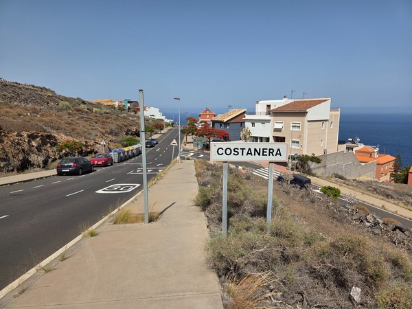 Ortsschild Costanera an der Küstenstraße mit Blick zum Meer im Hintergrund.