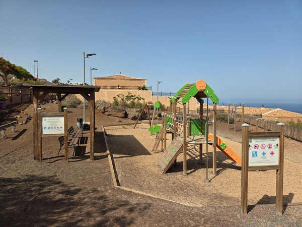 Spielplatz in Costanera mit Kletterelementen aus Holz und Meeresblick im Hintergrund.