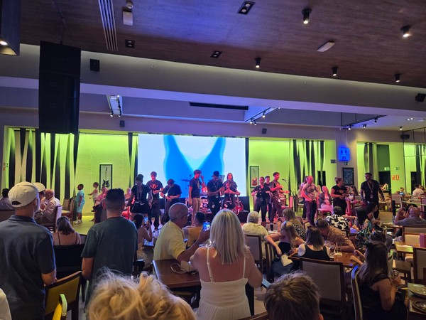 Mehrere Sängerinnen und Sänger stehen gemeinsam auf der Bühne des Hard Rock Cafe Tenerife und animieren das Publikum.