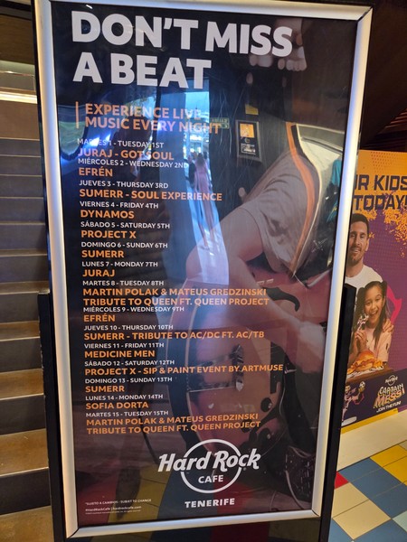 Plakat im Hard Rock Cafe Tenerife mit dem Monatsprogramm 'Don't Miss a Beat' und täglichen Live-Acts.