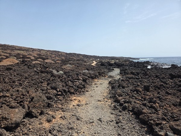 Schmaler Wanderpfad nahe der Küste; links und rechts dunkle, brüchige Lavabrocken im Malpaís de Güímar.