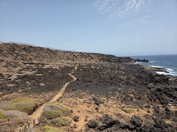Weitwinkliger Überblick über den Küstenpfad im Malpaís de Güímar: ein heller, schmaler Trail schlängelt sich durch schwarze Lavafelder bis zur schroffen Atlantikküste.
