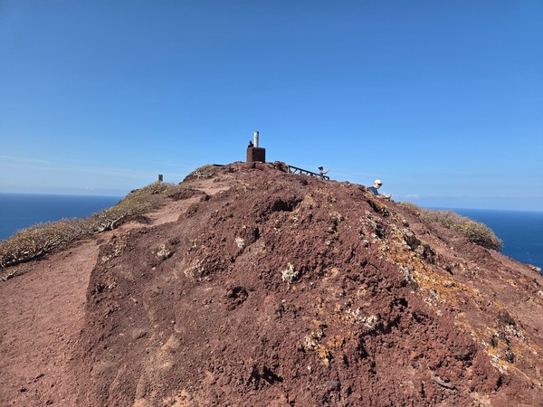 Schmaler Gipfelgrat der Montaña Roja mit Peilstein und Besuchern über dem Atlantik.