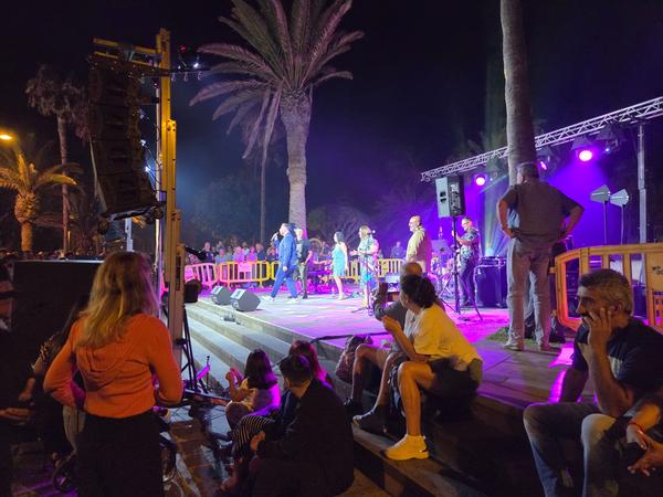 Live-Band tritt auf einer beleuchteten Bühne unter Palmen auf, begleitet von einem tanzenden Publikum.