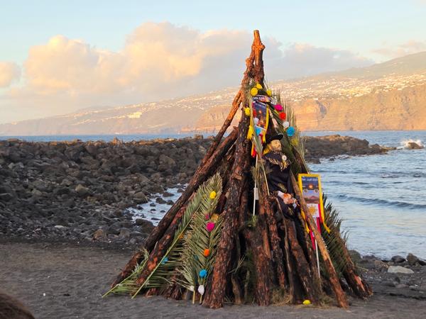 Aufgeschichtetes Holz mit einer dekorierten Figur und Palmblättern – die zentrale Hoguera für das Feuer.