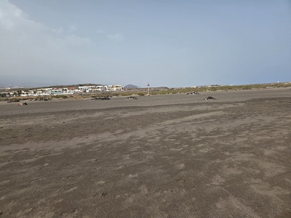 Weite, nahezu menschenleere Sandfläche der Playa de La Tejita mit einzelnen Steinhaufen in der Düne.