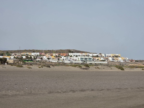 Blick auf die nahe Wohnsiedlung bei La Tejita mit mehrstöckigen Häusern und einer vorbeifahrenden grünen Titsa-Buslinie.