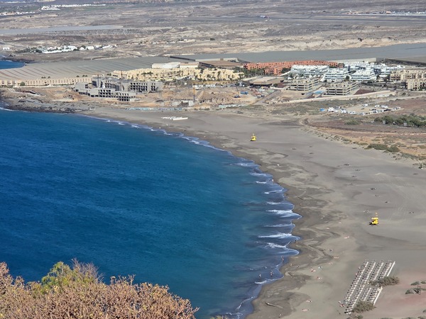 Panoramablick von der Montaña Roja über die gesamte Playa de La Tejita mit breitem Strand und gelben Rettungstürmen.